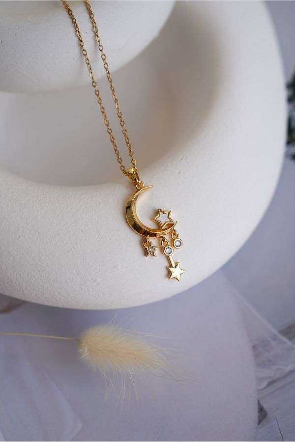 Gold necklace with a moon and star pendant on a white stand.